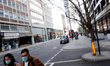 A couple wearing masks walk along a near-deserted Tottenham Court Road in London, England,...