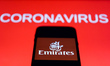 Emirates app icon is seen on the smartphone screen with coronavirus sign in the background...