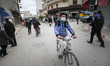 A young man wearing a protective face mask as he rides a bicycle in the street of Ariana d...