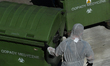 A worker wearing protective suit, helmet and mask, collects bins with medical waste at the...