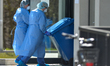 Medical workers wearing protective suits, helmets and masks, push empty bins at the entran...