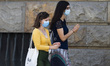 Two girls with mask walks through the city and disinfect the hands during the life normali...