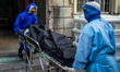 Funeral workers wearing personal protective equipment (PPE) carry a body to a crematorium...