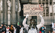 A man with gas mask and protective suits holds a placard ''protect the virus of Nazi'' is...