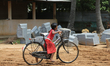 Tamil girl rides her bicycle past large stones waiting to be carved during re-construction...