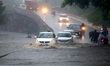 Indian People drives through a flooded road during a Heavy Monsoon Rain shower in Ajmer, R...