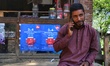 A man speaks on a mobile phone with reliance Jio poster installed on the counter of a shop...