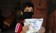 A boy clad in mask due to the COVID-19 coronavirus pandemic stands holding a bag of powder...