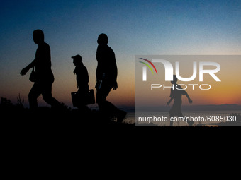 Silhouettes of walking refugees and migrants on the hills early in the morning during the dawn and the sunrise over the Aegean sea and Turke...