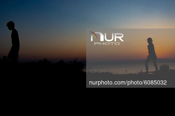 Silhouettes of walking refugees and migrants on the hills early in the morning during the dawn and the sunrise over the Aegean sea and Turke...