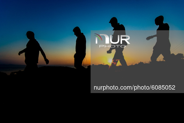 Group of male asylum seekers walk early in the morning towards Moria. Silhouettes of walking refugees and migrants on the hills early in the...