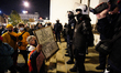 A woman holds a sign with the words "This is war" in front of riot police at the Three Cro...