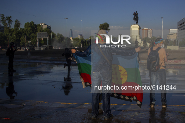 A person holds a Mapuche flag, after being wet by the cart throws water from the riot police of carabineros de Chile (COP) on October 30, 20...