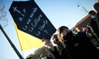 A young woman holds a placard depicting a coffin and reading 'RIP the social life? The cul...