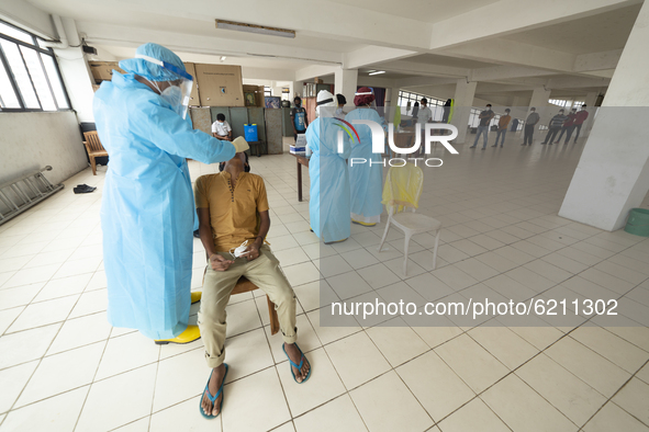 A Sri Lankan Health worker in a protective suit takes a throat swab of a man for a COVID-19 test as people line up for their tests  at Colom...