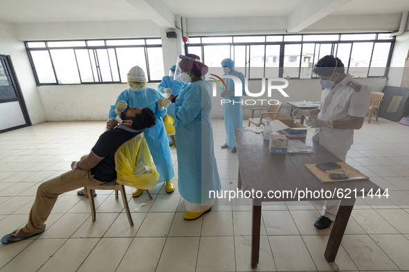 A Health worker in a protective suit  takes a throat swab of a man for a COVID-19 test as other health officials assist at Colombo, Sri Lank...