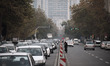 An Iranian woman wearing a protective face mask crosses an avenue as vehicles stoped behin...