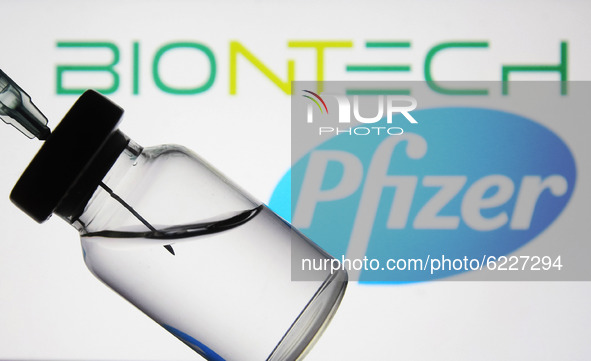 A medical syringe and a vial in front of the Pfizer US pharmaceutical corporation and Biontech German biotechnology company logos are seen i...