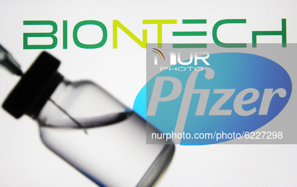 A medical syringe and a vial in front of the Pfizer US pharmaceutical corporation and Biontech German biotechnology company logos are seen i...