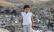 Portrait of a little Syrian girl posing in front of the burnt makeshift refugee camp in th...