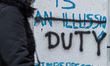 A Passers-by in protective face masks  is seen walking by a graffiti on a cold winter even...