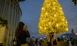 A women takes a photo of women wearing face mask while standing under a Christmas tree on...