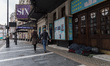 A couple walks past a homeless person seeking shelter in a doorway of a closed theatre in...