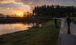 People and dogs as seen outside for a morning walk. Sunrise sky ovre the lake with reflect...