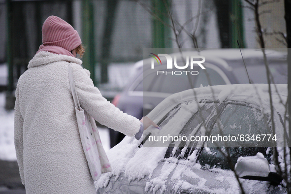 A woman scrapes snow from a car window in the Royal Baths park in Warsaw, Poland on January 13, 2021. Though temperatures normally reach bel...