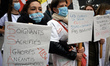 A nurse holds a placard reading 'Nurses sacrified, ignored, destroyed, and without conside...