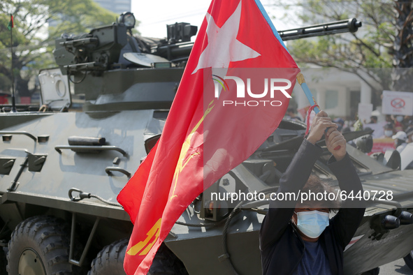 A Myanmar protester waves a National League for Democracy ( NLD ) party flag in front of an armoured vehicle during a demonstration against...