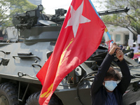 A Myanmar protester waves a National League for Democracy ( NLD ) party flag in front of an armoured vehicle during a demonstration against...