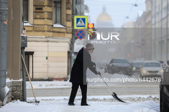 A woman cleans the street from snow after a heavy snowfall in St. Petersburg, Russia, on February 16, 2021. 
