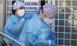 Two health workers put their protective suits before administering COVID-19 vaccines to se...