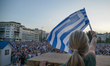 A woman waves the Greek flag outside the Greek Parliament in central Athens during a mass...