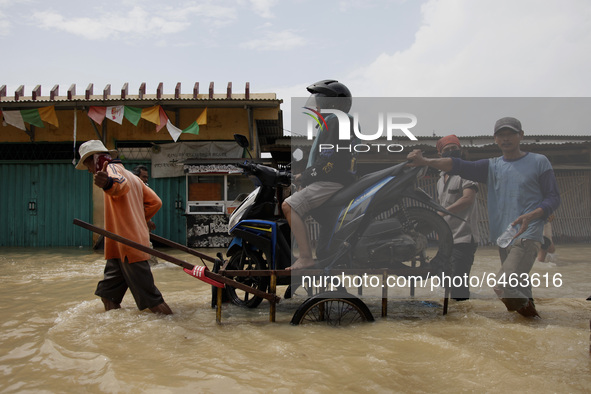 a woman sit on her motorbike carried by a cart service as she crosses the flood in Pebayuran sub-district, Bekasi regency, West Java, on Feb...