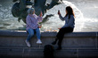 Women take photos beside one of the fountains of Trafalgar Square in mild spring weather i...