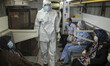 A health assistant wearing a protective suit looks on as people who have infected by the C...