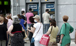 People wait in line at an ATM outside a National bank branch in a neighborhood at Ilioupol...