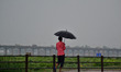 An indian pedestrain uses an umbrella to shelter from rain as he walks along a road,in All...