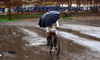 An Indian cyclist uses an umbrella  to shelter from rain,in Allahabad on June 29,2015. 