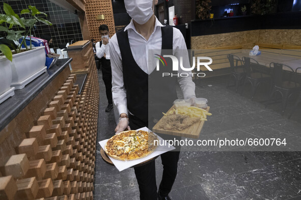 An Iranian waiter wearing a protective face mask scarves fast-food for a family in the holy city of Qom, 145Km (90 miles) south of Tehran, a...