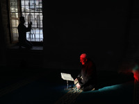 A Palestinian elder reads from the Quran as a Palestinian prays before breakfast in Al-Omari mosque during the Muslim holy month of Ramadan,...