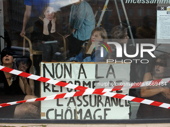 Dancers stand inside a store front with a placard reading 'No to the unemployment benefits reform'. Disguised culture workers (actors, live...