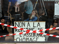 Dancers stand inside a store front with a placard reading 'No to the unemployment benefits reform'. Disguised culture workers (actors, live...
