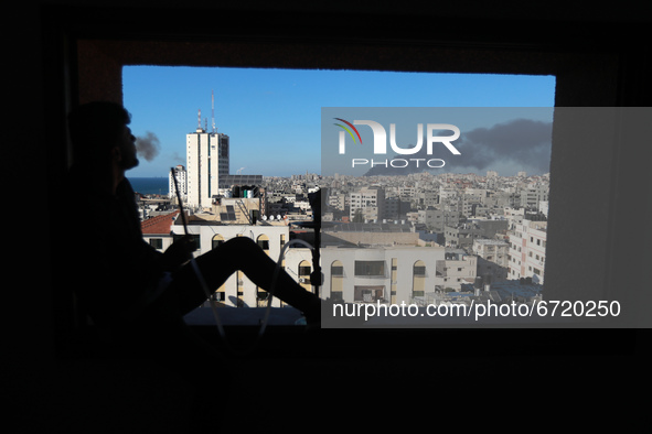 A Palestinian man smokes a waterpipe (shisha or hookah) as the rockets and smoke rises amid a flare-up of Israeli-Palestinian violence, in G...