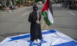 A protester carries a Palestinian flag while standing on an Israeli flag while participati...