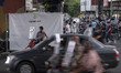 An Iranian motor taxi driver sits on his motorcycle in front of a banner that has located...