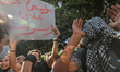 A protester raises a placard that reads in Arabic using swear words and profanity, ‘you ma...