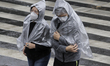 Two passers-by take cover from the rain with raincoats in the Historic Centre of Mexico Ci...